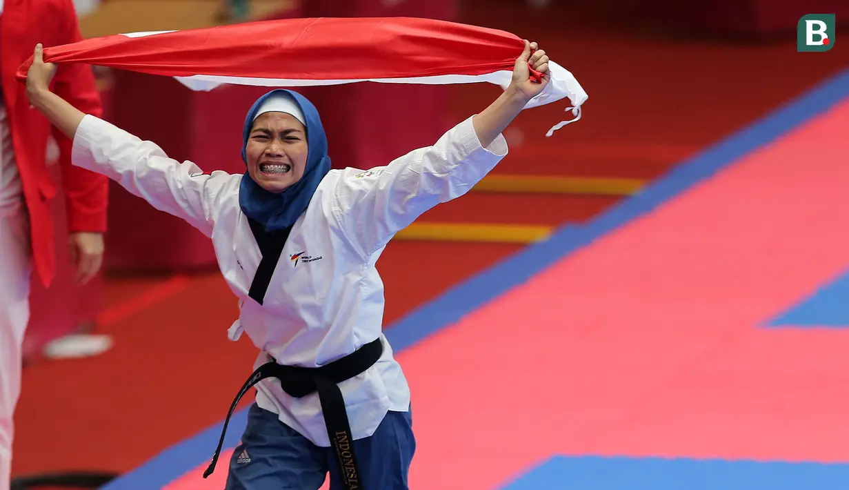 Atlet taekwondo, Defia Rosmaniar, melakukan selebrasi usai berhasil meriah medali emas pertama untuk Indoensia di Asian Games 2018 di JCC, Jakarta, Minggu (19/8/2018). (Bola.com/Peksi Cahyo)