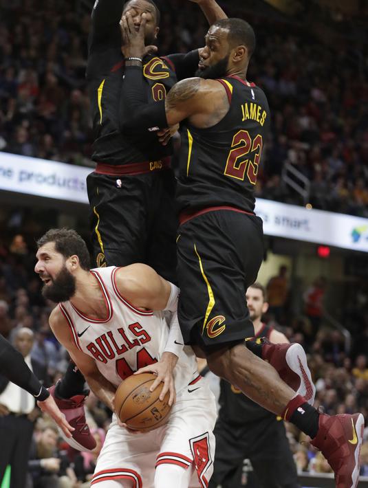 Pemain Chicago Bulls, Nikola Mirotic (bawah) berusaha memasukan bola saat dikepung dua pemain Cleveland Cavaliers pada laga NBA basketball game di Quicken Loans Arena, Cleveland, (21/12/2017). Cleveland menang 115-112.  (AP/Tony Dejak)