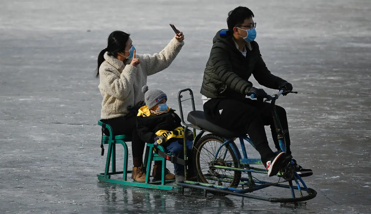 Sebuah keluarga menggunakan ponsel untuk berswafoto saat menaiki kereta luncur di danau beku di Beijing pada Selasa (12/1/2021). Ketika musim dingin tiba, danau di Beijing banyak yang membeku dan dijadikan area ice skating musiman. (Photo by WANG Zhao / AFP)