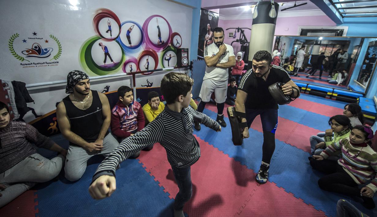 Pengungsi Suriah Amir al-Awad (kaos putih) memperhatikan siswanya berlatih di Akademi Olahraga Suriah di Alexandria, Mesir (4/1). Akademi ini menjadi tempat latihan khususnya anak-anak untuk belajar bela diri. (AFP/Khaled Desouki)