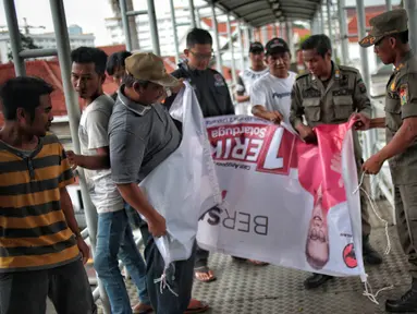 Petugas Satpol PP menertibkan alat peraga kampanye (APK) di jembatan penyeberangan orang (JPO) kawasan Gambir, Jakarta, Sabtu  (22/12). Penertiban itu dilakukan karena melanggar aturan pemasangan dari komisi pemilihan umum. (Liputan6.com/Faizal Fanani)