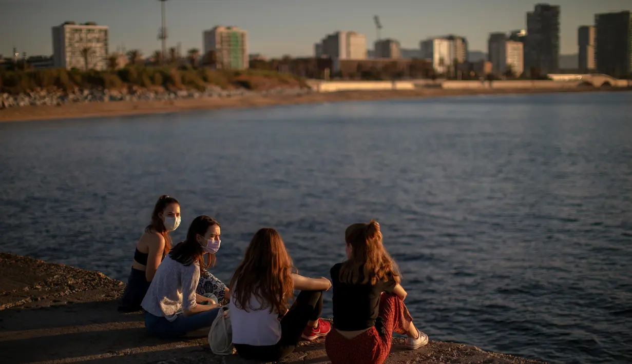 Sejumlah wanita mengenakan masker duduk di depan laut di Barcelona, Spanyol, Rabu, (20/5/2020). Berjemur dan berenang masih tidak diizinkan di pantai tersebut.  (AP Photo/Emilio Morenatti)