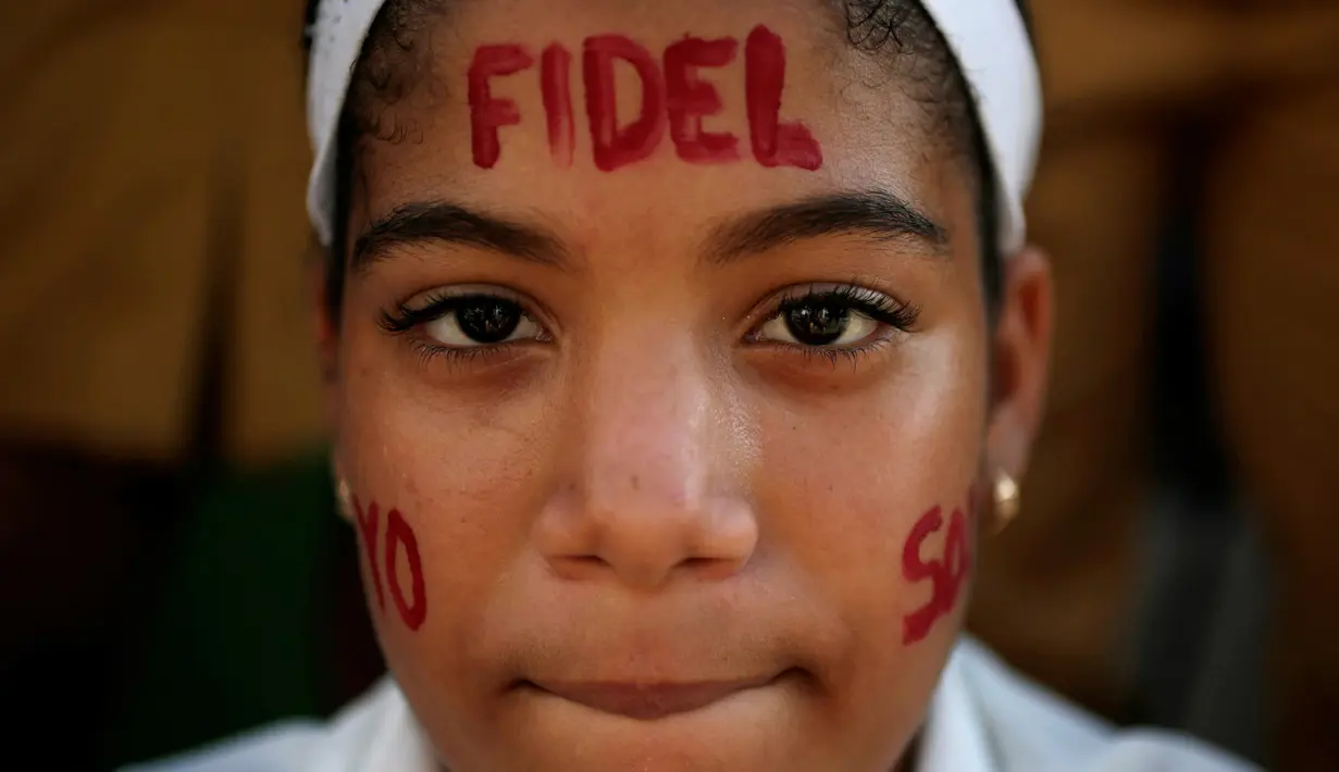 Seorang anak melukis wajah mereka dengan tulisan Fidel saat menunggu mobil yang membawa abu mantan pemimpin Revolusi Kuba, Fidel Castro, lewat di Bayamo, Kuba (3/11). (Reuters/Enrique De La Osa)