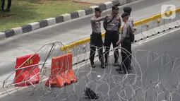 Personel Kepolisian berjaga dibalik barikade kawat berduri yang menutup ruas Jalan Medan Merdeka Barat, Jakarta, Senin (28/10/2019). Penutupan ini antisipasi aksi unjuk rasa mahasiswa mendesak Presiden Jokowi segera mengeluarkan Perppu KPK. (Liputan6.com/Helmi Fithriansyah)