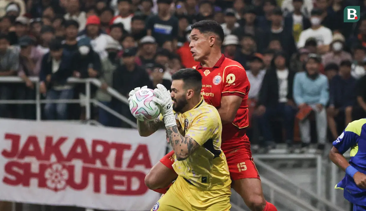 Van Basty Sousa (kanan) berduel dengan kiper Arema FC, Lucas Frigeri dalam laga persahabatan yang diselenggarakan di markas kebanggaan Macan Kemayoran, Jakarta International Stadium (JIS), Sabtu (26/7/2025). (Bola.com/Abdul Aziz)