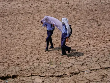 Anak-anak sekolah menggunakan handuk katun di atas kepala mereka untuk melindungi diri dari terik matahari saat berjalan melintasi ladang kering di pinggiran Jammu, India, Rabu 20 Mei 2026. (AP Photo/Channi Anand)