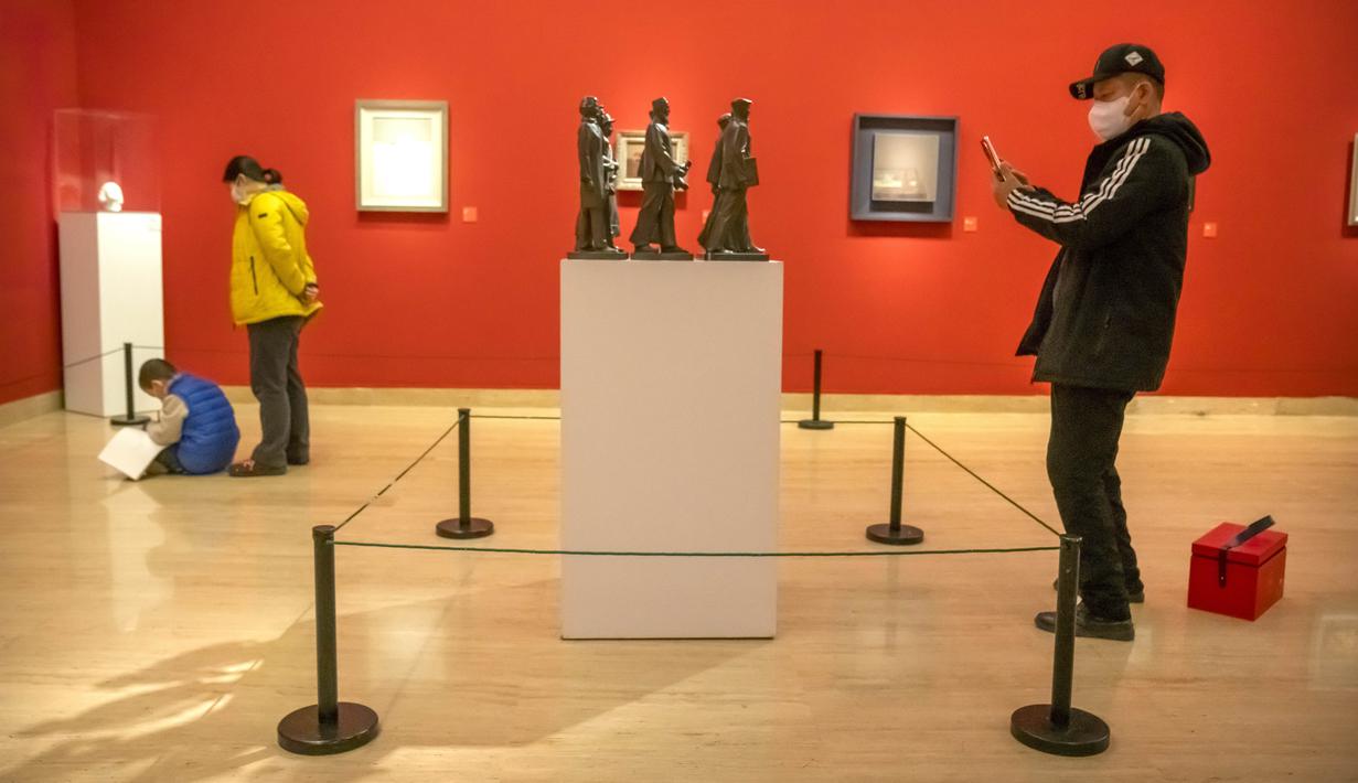 Seorang pria yang mengenakan masker mengambil foto sebuah patung di sebuah galeri di Museum Seni Nasional China di Beijing, Rabu (1/2/2023). Pengunjung terus berduyun-duyun ke museum, situs bersejarah, dan tempat wisata di ibu kota China saat periode liburan Tahun Baru Imlek berakhir. (AP Photo/Mark Schiefelbein)