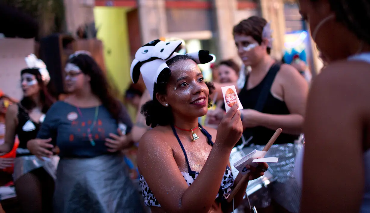 Seorang wanita membagikan stiker saat merayakan karnaval "Maria vem com as outras" di Rio de Janeiro, Brasil (3/2). Karnaval ini digelar agar mendorong wanita di Brasil melaporkan pelecehan jika terjadi pada mereka. (AP Photo / Silvia Izquierdo)