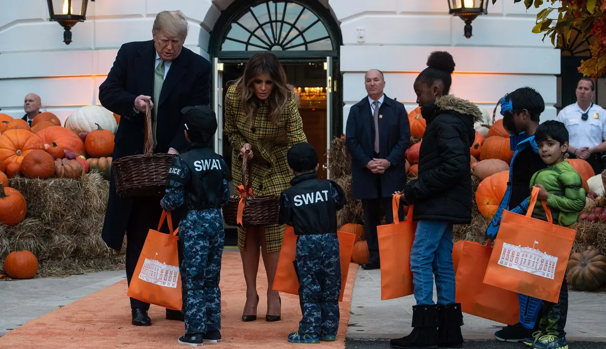 Presiden Amerika Serikat (AS) Donald Trump dan Ibu Negara Melania Trump membagikan permen kepada anak-anak selama yang hadir acara trick-or-treat pada perayaan Halloween di Gedung Putih, Washington, Minggu (28/10). (NICHOLAS KAMM / AFP)