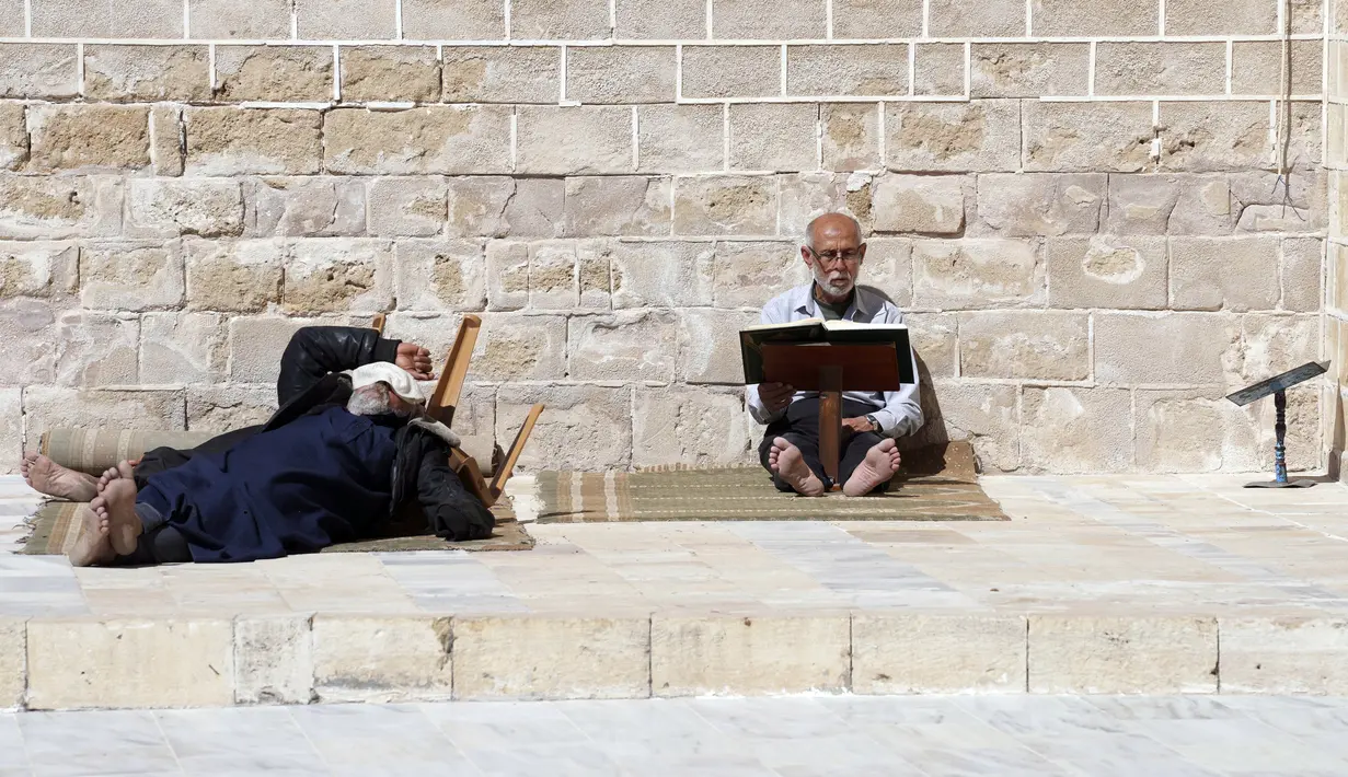 Seorang pria membaca ayat-ayat Alquran sementara pria lain beristirahat dekatnya saat mereka menunggu waktu berbuka puasa selama bulan suci Ramadhan di Masjid Al-Omari, Kota Gaza, Palestina, 13 April 2022. (AP Photo/Adel Hana)