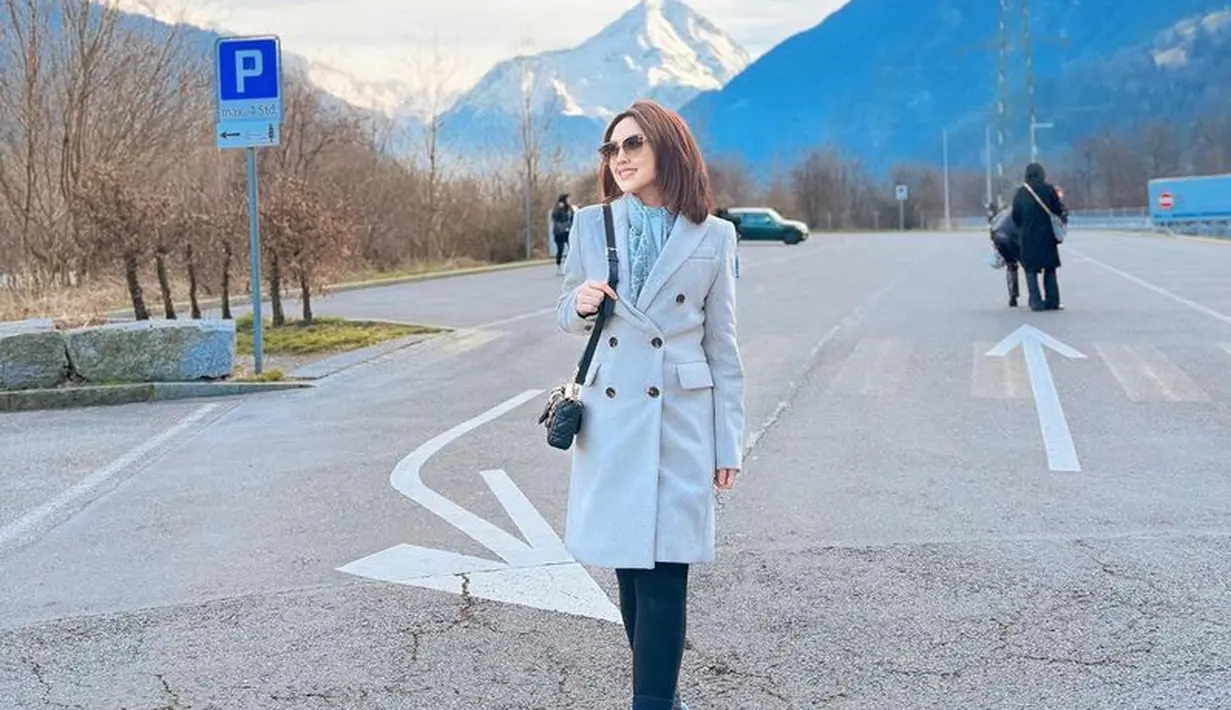 Happy Asmara tampil dengan coat panjang model blazer warna silver dipadukan celana ketat hitam dan sneakers putihnya. [@happy_asmara77]