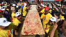 Peserta menunjukan pizza yang telah selesai dibuat di jalur Auto Club Speedway, di Fontana, California (10/6). Mereka berhasil memecahkan rekor Guinness World Records untuk pizza terpanjang di dunia dengan panjang 1,32 mil atau 2,13 km. (AFP/Mark Ralston)