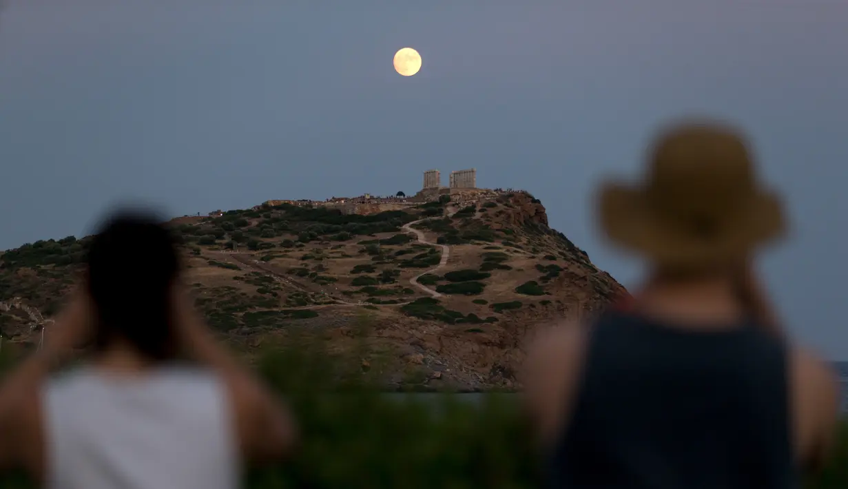 Pengunjung menyaksikan pemandangan bulan purnama hampir penuh yang menampakkan diri di langit Kuil Poseidon kuno di Cape Sounion, sekitar 70 kilometer sebelah tenggara Athena, Yunani (2/8/2020). (Xinhua/Marios Lolos)