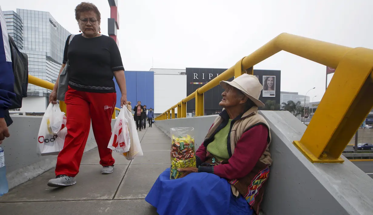 Warga berjalan di dekat Alejandra Baldani, nenek 78 tahun yang berjualan permen di jembatan penyeberangan di distrik San Borja, Lima, 22 Oktober 2015. Nenek Baldani mendapatkan sekitar USD 3 per hari dari hasil berjualan permen. (REUTERS/Mariana Bazo)