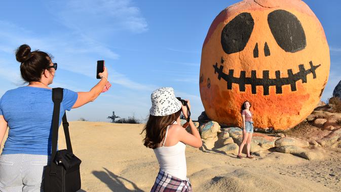 Orang-orang mengunjungi Pumpkin Rock (Batu Labu) di puncak sebuah bukit di Norco,  California, AS (18/10/2020). Menjelang perayaan Halloween, Pumpkin Rock, sebongkah batu raksasa yang dilukisi seperti Jack-O'-Lantern besar, menjadi objek wisata yang populer bagi pengunjung. (Xinhua/Gao Shan)