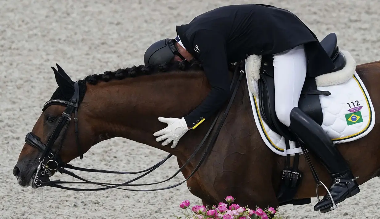 Selebrasi Joao Victor Marcari Oliva dari Brasil, memeluk kuda yang ia tunggangi usai bertanding dalam kategori Tunggang Serasi Berkuda dalam Olimpiade Tokyo 2020 di Equestrian Park, Tokyo, Sabtu (24/7/2021). (Foto: AP/Carolyn Kaster)