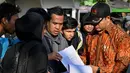 Sementara itu, terdapat empat WNI yang telah kembali ke Indonesia secara mandiri pada Selasa pagi (20/1/2026). Tampak dalam foto, orang-orang memeriksa nama mereka di daftar di depan Kedutaan Besar Republik Indonesia (KBRI) di Phnom Penh, Kamboja, pada Rabu 21 Januari 2026. (TANG CHHIN Sothy/AFP)