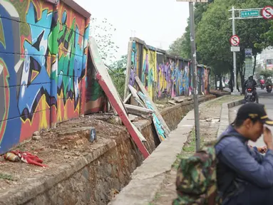 Seorang pria duduk di dekat tembok Jalan Juanda yang ambruk di kawasan Depok, Jawa Barat, Senin (2/12/2019). Kondisi tembok yang dipenuhi mural tersebut mulai rapuh dan sebagian sisinya telah ambruk serta miring sehingga membahayakan pejalan kaki. (Liputan6.com/Immanuel Antonius)