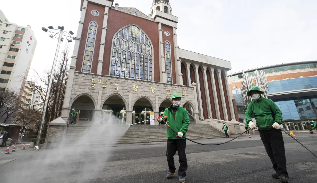 Pekerja memakai masker menyemprotkan disinfektan sebagai tindakan pencegahan virus corona COVID-19 di depan Katedral Myeongdong di Korea Selatan, Rabu, (26/2/2020). Total kasus Virus Corona COVID-19 Korea Selatan melonjak menjadi empat angka pada Rabu 26 Februari 2020. (Yun Dong-jin/Yonhap via AP)