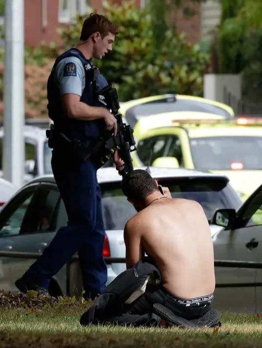 Seorang pria menggunakan telepon genggamnya dekat polisi bersenjata setelah insiden penembakan di Masjid Al Noor, Christchurch, Selandia Baru, Jumat (15/3). (AP Photo/Mark Baker)