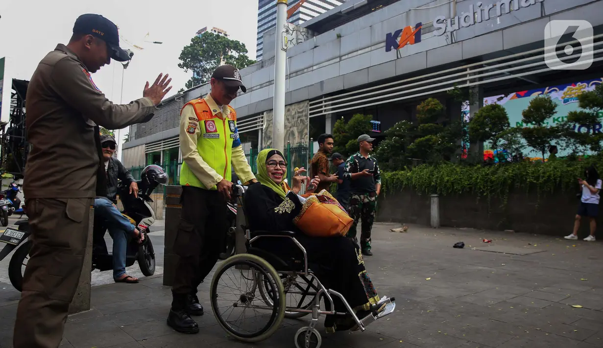 Petugas keamanan KAI Commuter Line membantu seorang calon penumpang lanjut usia (lansia) untuk masuk ke dalam Stasiun Sudirman, Jakarta, Selasa (10/12/2024). (Liputan6.com/Angga Yuniar)
