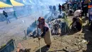 Seorang peserta mengipasi api saat memasak lemang, hidangan nasi ketan tradisional yang dimasukkan ke dalam tabung bambu dan diisi dengan santan yang kemudian diletakkan di atas api terbuka, selama acara memasak massal di Blang Pidie, Kabupaten Aceh Barat Daya, Aceh, pada Sabtu 25 April 2026. (CHAIDEER MAHYUDDIN/AFP)