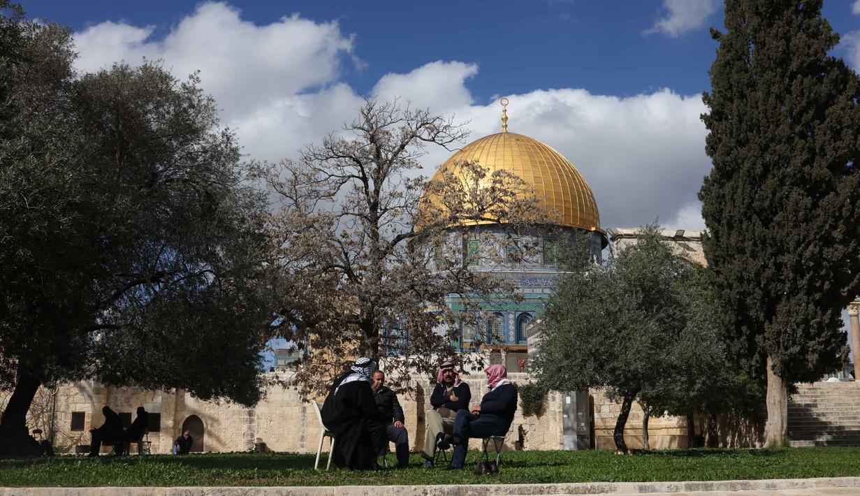 Para pria Palestina duduk di dekat Kubah Batu, kompleks Masjid al-Aqsa, Yerusalem menjelang waktu berbuka puasa selama bulan suci Ramadan 1447 Hijriah pada Rabu 25 Februari 2026. Kubah Shakhrah atau Dome of the Rock atau Qubbat as-Sakhrah merupakan ikon di kompleks Masjid Al Aqsa. (AHMAD GHARABLI/AFP)