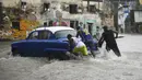 Sejumlah pria mendorong mobil tua Amerika Serikat di jalan yang banjir di Havana, Kuba, 30 Juni 2021. Hujan deras dan selokan yang tidak berfungsi menyebabkan banjir di jalan-jalan di Havana. (YAMIL LAGE/AFP)