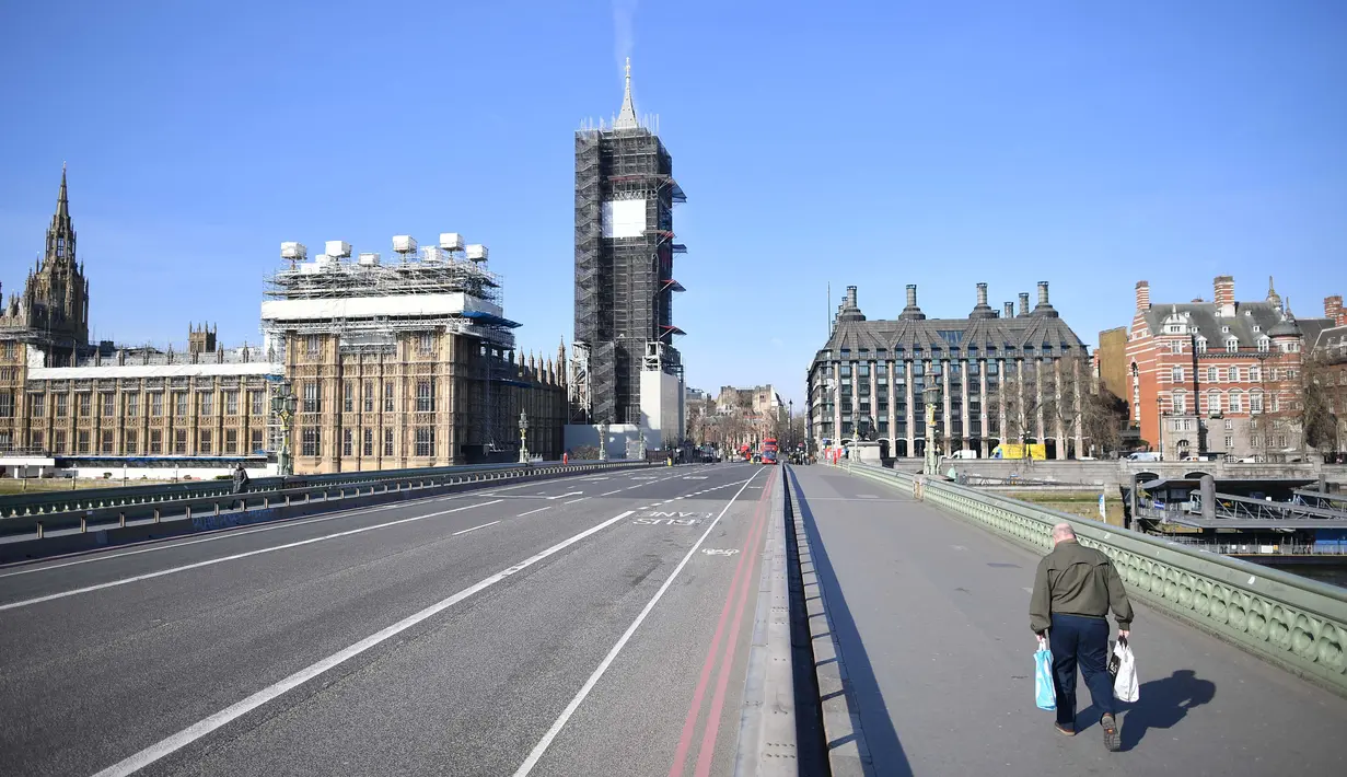 Sebuah gambar menunjukkan Gedung Parlemen (kiri) di ujung Westminster Bridge yang kosong dengan seorang pejalan kaki di trotoar London setelah pemerintah Inggris setempat memberlakukan lockdown akibat pandemi Covid-19 pada 24 Maret 2020. (Photo by JUSTIN TALLIS / AFP)