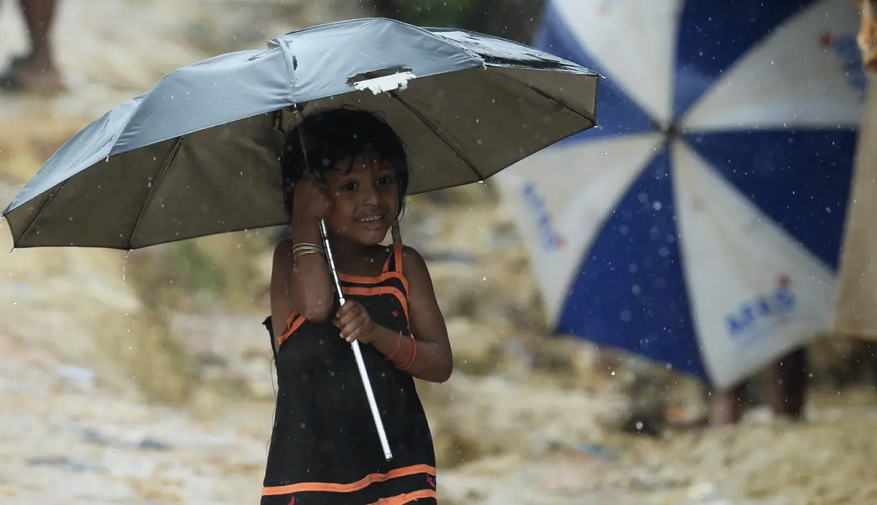 Seorang anak pengungsi Rohingya berjalan menggunakan payung saat hujan di kamp pengungsi Kutupalong, Ukhia (12/9/2019). Kamp ini didirikan secara tidak resmi pada tahun 1991, setelah ribuan orang Rohingya melarikan diri dari Operasi Pyi Thaya yang dilancarkan militer Burma. (AFP Photo/Munir Uz Zaman