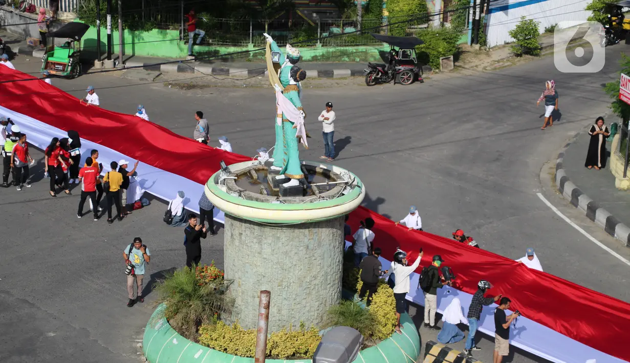 Pelajar SMA membentangkan bendera Merah Putih sepanjang 2,3 kilometer di Jalan Panjaitan dan Jalan Nani Wartabone, Gorontalo, Kamis (23/1/2020). Sebanyak 2.300 pelajar SMA berpartisipasi dalam acara tersebut dengan ikut memegang bendera. (Liputan6.com/Arfandi Ibrahim)