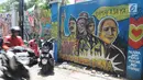 Pengendara motor melintasi mural pemilu di Jalan Karet, Depok, Jawa Barat, Rabu (20/3). Mural tersebut mengajak masyarakat untuk berpartisipasi dalam menyukseskan pemilu dengan cara damai dan menjaga meski berbeda pilihan. (Liputan6.com/Herman Zakharia)