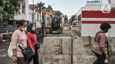 Pejalan kaki saat melintas di dekat proyek revitalisasi pedestrian kawasan Kota Tua, Jakarta, Minggu (27/3/2022). Jalur pedestrian itu akan diubah menjadi plaza pedestrian yang lebar sebagai bagian dari penataan kawasan Kota Tua yang rendah emisi (merdeka.com/Iqbal S Nugroho)