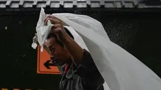 Seorang pria berlindung dari hujan dengan selembar plastik di Beijing, Minggu (30/7/2023). China menempatkan sebagian wilayah utara negara tersebut dalam keadaan siaga merah, termasuk wilayah Beijing, karena hujan lebat yang diperkirakan akan terjadi akibat datangnya topan Doksuri, yang saat ini menghantam bagian lain negara tersebut. (Pedro PARDO / AFP)