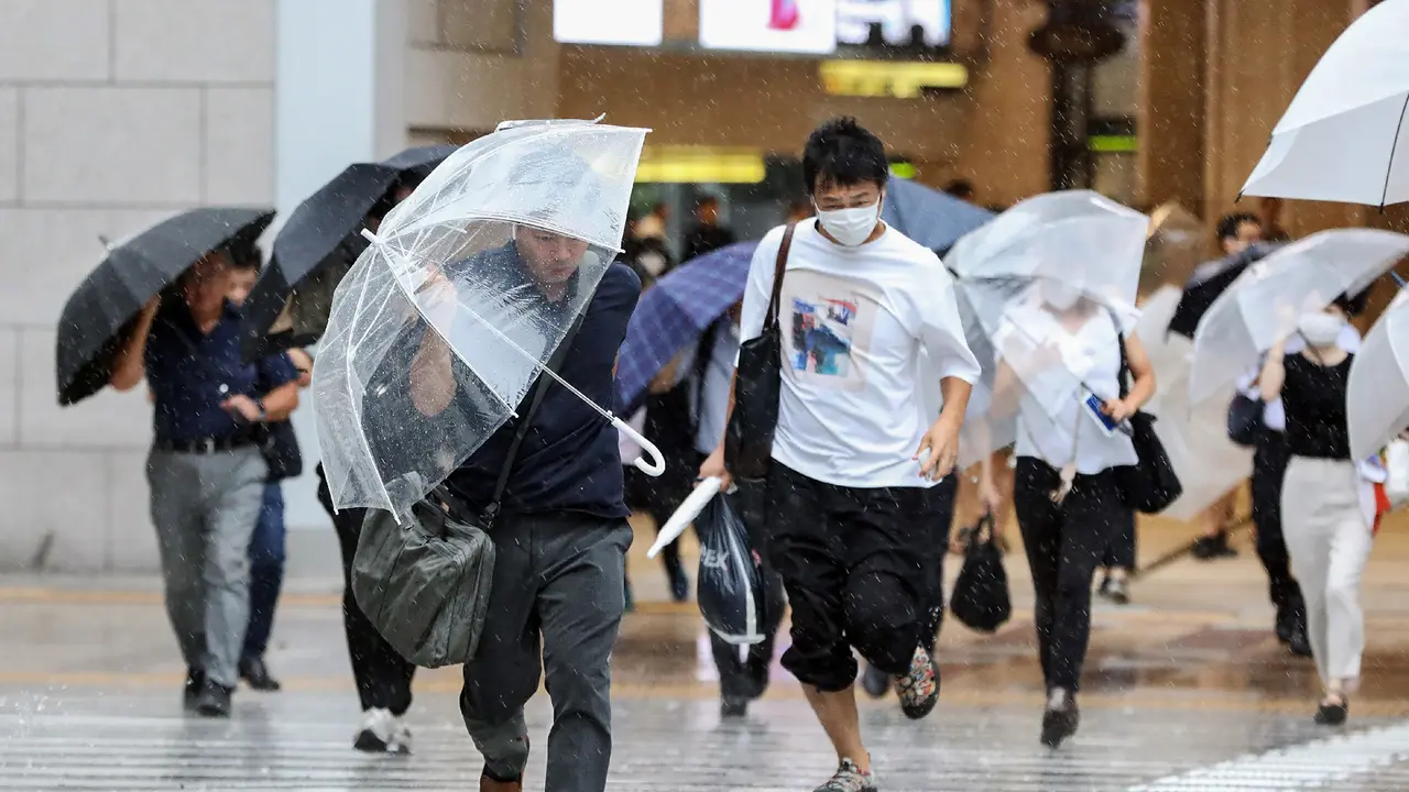 Pejalan kaki mencoba berlindung dari angin dan hujan saat mereka menyeberang jalan di depan Stasiun Osaka pada 15 Agustus 2023, saat Badai Tropis Lan menerjang pulau utama Honshu pada malam hari.