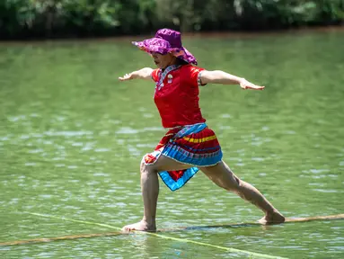 Seorang perempuan melakukan aksi meniti satu bambu di atas air di Chishui, Provinsi Guizhou, China pada 25 Juni 2020. Seni meniti satu bambu berasal dari Guizhou ini mengharuskan seseorang untuk berdiri atau duduk di atas sebatang bambu sembari melakukan gerakan keseimbangan. (Xinhua/Tao Liang)