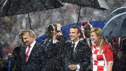 Presiden Rusia Vladimir Putin (kiri) bersama Presiden Prancis Emmanuel Macron (tengah) dan Presiden Kroasia Kolinda Grabar-Kitarovic berjalan dalam hujan usai laga final Piala Dunia 2018 di Stadion Luzhnik, Moskow, Rusia, Minggu (15/7). (Franck Fife/AFP)