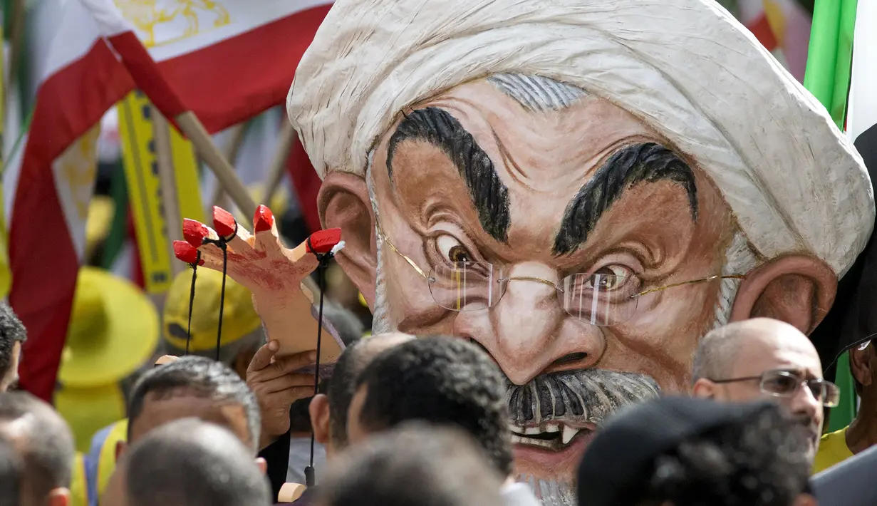 Max Saatchi bersama pengunjuk rasa lainnya sambil mengenakan topeng Presiden Iran Hassan Rouhani saat mengecam pelanggaran hak asasi manusia oleh pemerintah Rouhani di luar markas besar PBB, Manhattan, New York, AS (28/9/2015). (REUTERS/Darren Ornitz)