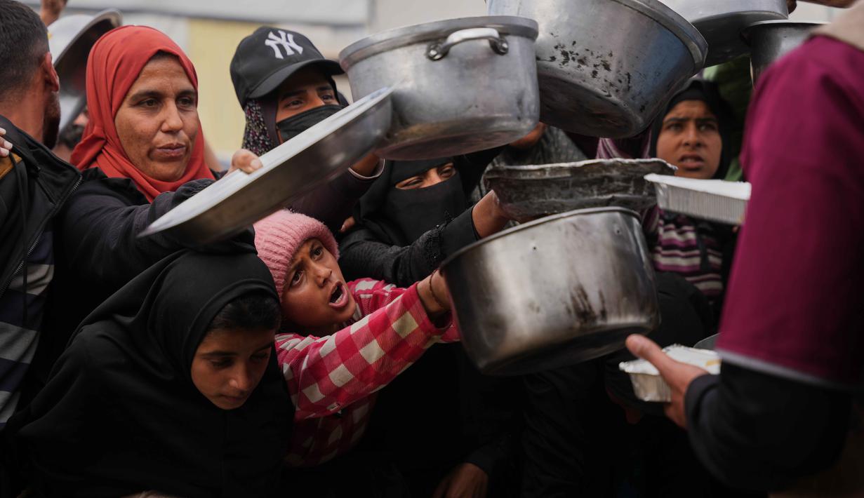 Melalui platform media sosial X, pada Kamis (5/2/2026), UNRWA mengatakan bahwa pengiriman bantuan kemanusiaan, termasuk makanan, perlengkapan kebersihan, obat-obatan, dan perlengkapan tempat tinggal, tetap disimpan di gudang-gudang di Mesir dan Yordania dan belum diizinkan masuk ke Gaza selama berbulan-bulan. Tampak dalam foto, warga Palestina berebut menerima makanan sumbangan di dapur umum, Khan Younis, Jalur Gaza selatan, Jumat 6 Februari 2026. (AP Photo/Abdel Kareem Hana)
