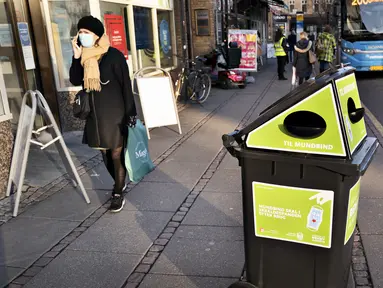 Seorang pejalan kaki berjalan melewati tempat sampah untuk masker sekali pakai, di Aarhus Center, Denmark, Senin (23/11/2020). Kota Aarhus menempatkan seratus tempat sampah khusu berukuran 240 liter yang dapat menampung sekitar 3000 masker bekas. (Henning Bagger/Ritzau Scanpix/AFP)