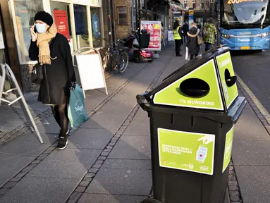 Seorang pejalan kaki berjalan melewati tempat sampah untuk masker sekali pakai, di Aarhus Center, Denmark, Senin (23/11/2020). Kota Aarhus menempatkan seratus tempat sampah khusu berukuran 240 liter yang dapat menampung sekitar 3000 masker bekas. (Henning Bagger/Ritzau Scanpix/AFP)