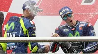 Pembalap Movistar Yamaha, Maverick Vinales merayakan kemenangannya setelah finis pertama pada MotoGP Argentina dengan menyemprotkan sampanye bersama Valentino Rossi di atas podium Sirkuit Termas de Rio Hondo, Minggu (9/4). (AP Photo/Nicolas Aguilera)