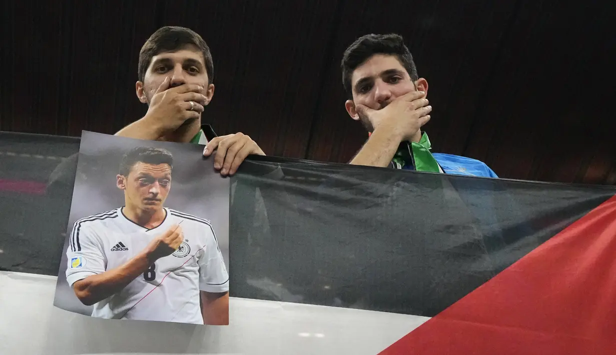 Penonton memegang foto pemain sepak bola timnas Jerman Mesut Ozil di tribun pada akhir pertandingan Spanyol vs Jerman saat laga Grup E Piala Dunia 2022  di Stadion Al Bayt, Kota Al Khor pada Senin (28/11/2022) dini hari WIB. Sambil memegang foto Mesut Ozil, para penonton berpose sambil menutup mulut dengan tangan mereka. (AP Photo/Julio Cortez)