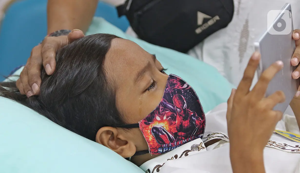 Seorang anak bermain gadget saat melakukan operasi sunat di Puskesmas Kecamatan Cilandak, Jakarta, Kamis (2/12/2021). Sebanyak 50 anak mengikuti kegiatan sunat massal secara gratis dalam rangka Hari Kesehatan Nasional ke-57 mulai Selasa (30/11) hingga Jumat (3/12). (Liputan6.com/Herman Zakharia