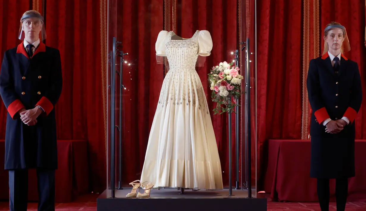 Petugas kerajaan berdiri di samping gaun pengantin Putri Beatrice yang dipajang di Kastil Windsor, Windsor, Rabu (23/9/2020). Beatrice menikah dalam balutan gaun pengantin dari era tahun 1960-an rancangan Norman Hartnell yang dipinjamkan sang nenek, Ratu Elizabeth II. (AP Photo/Kirsty Wigglesworth)
