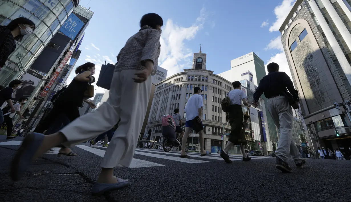 Warga yang mengenakan masker untuk membantu mengekang penyebaran COVID-19 berjalan di sepanjang penyeberangan pejalan kaki di Tokyo, Jepang, Selasa (27/7/2021). Tokyo melaporkan jumlah kasus harian COVID-19 tertinggi beberapa hari setelah Olimpiade dimulai. (AP Photo/Eugene Hoshiko)