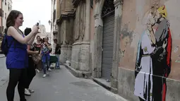 Pejalan kaki memotret mural Presiden AS, Donald Trump dan Paus Francis berciuman di sebuah dinding di Roma, Kamis (11/5). Dalam mural itu Fransiskus berpakaian putih dan memeluk Trump yang memiliki tanduk merah dan pistol. (AP Photo/Alessandra Tarantino)