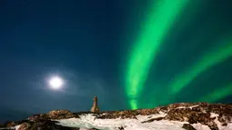 Fenomena ini terjadi ketika partikel bermuatan dari Matahari bertabrakan dengan medan magnet dan atmosfer bumi. Tampak dalam foto, Aurora Borealis menerangi langit malam di atas patung Hans Egede yang menghadap Nuuk, Greenland, pada 23 Januari 2026. (Jonathan NACKSTRAND/AFP)