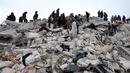 Warga dan tim penyelamat mencari korban dan orang yang selamat di antara puing-puing bangunan yang runtuh setelah gempa bumi di desa Besnaya, provinsi Idlib Barat Laut Suriah perbatasan dengan Turki, pada Senin 6 Februari 2022. Tim penyelamat di Turki dan Suriah menerjang cuaca yang sangat dingin, gempa susulan, dan bangunan yang runtuh, saat mereka menggali korban yang tertimbun oleh gempa bumi yang menewaskan lebih dari 5.000 orang. (OMAR HAJ KADOUR/AFP)
