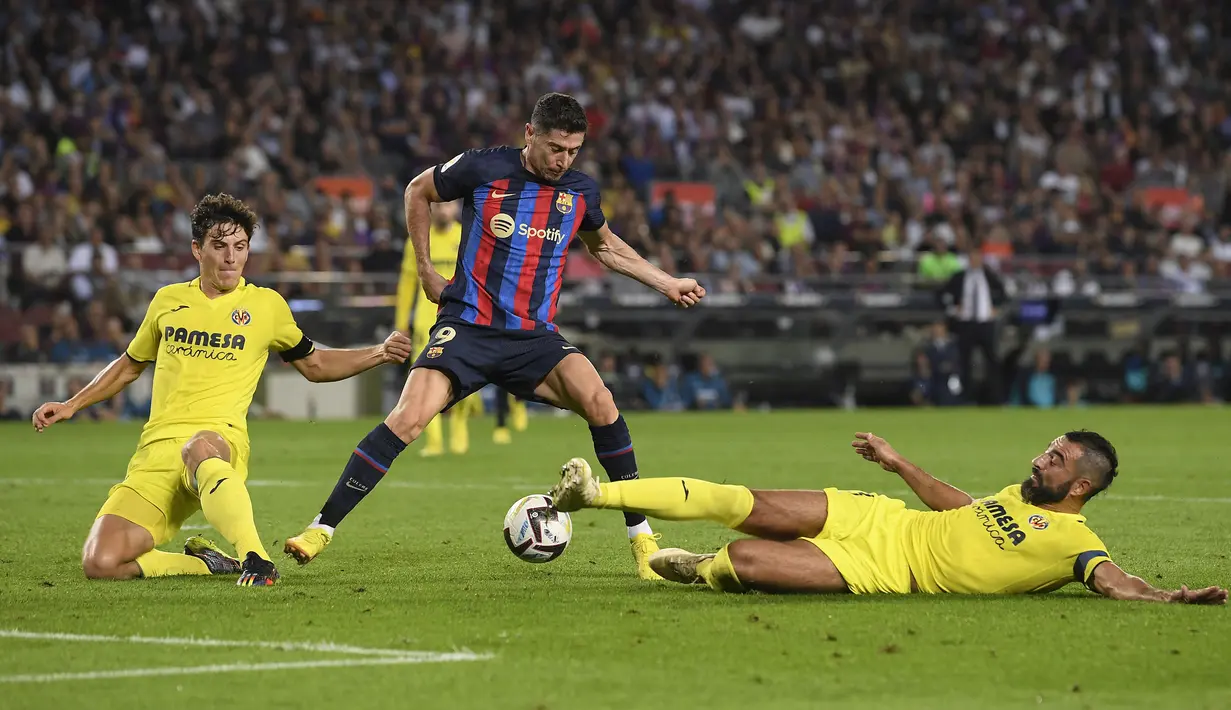 Pemain Barcelona, Robert Lewandowski (tengah) berebut bola dengan pemain Villarreal, Raul Albiol (kanan) pada laga lanjutan Liga Spanyol 2022/2023 di Stadion Camp Nou, Barcelona, 20 Oktober 2022. Pada musim ini, Lewandowksi berhasil mencetak 15 gol dan membuat dirinya tercatat sebagai top skor Liga Spanyol musim ini. (AFP/Josep Lago)